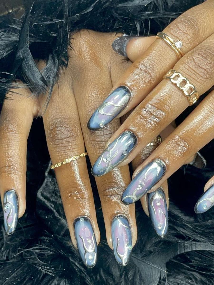 Ongles amande à effet chrome bleu-gris, reflets miroir marbrés, posés sur des plumes noires