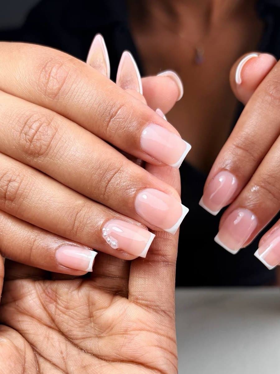 Deux mains en french blanche : ongles carrés sur l'une, stiletto sur l'autre, quelques fleurs blanches en relief
