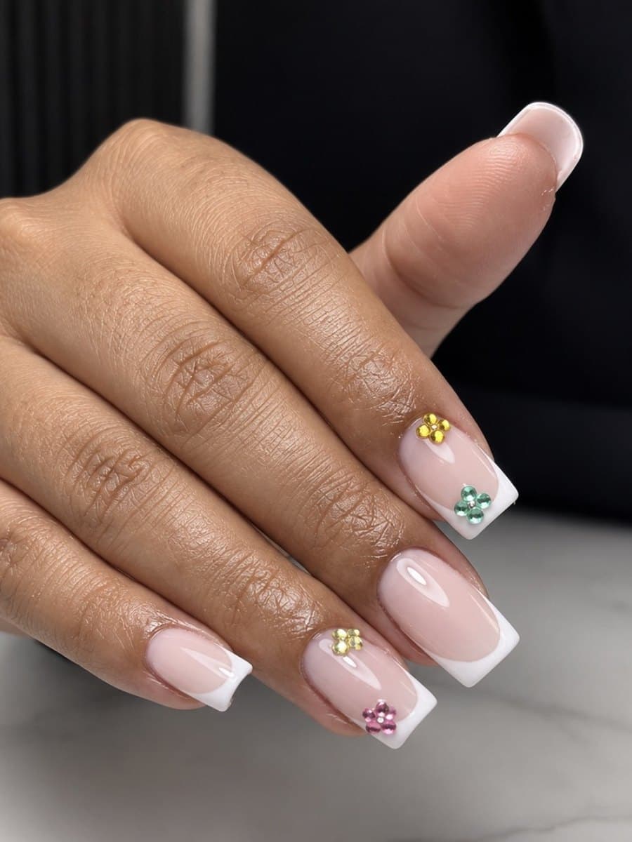 French blanche sur ongles carrés, petites fleurs de strass jaunes, vertes et roses posées sur la base