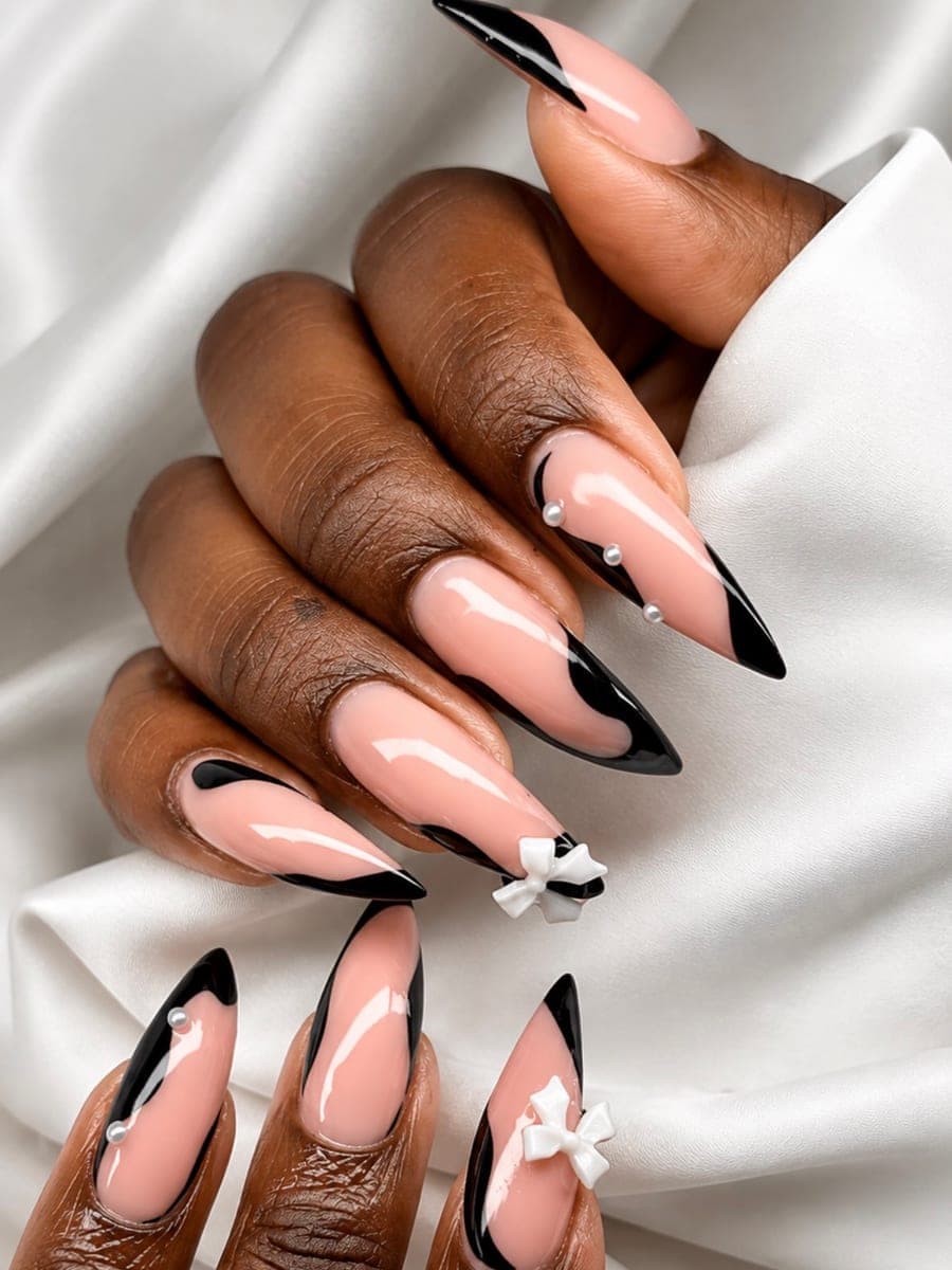 French noire sur ongles stiletto, ornée de perles blanches et de nœuds en relief