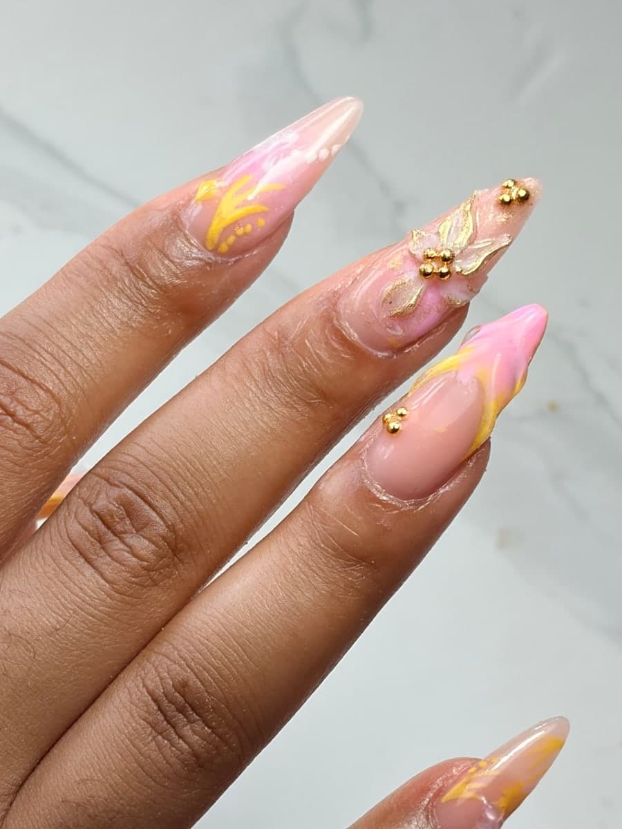 Ongles stiletto en marbrage rose et jaune, fleur dorée modelée en relief et perles dorées